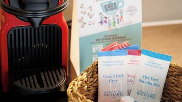 A red espresso machine, a basket with tea packets, and a sign with text.