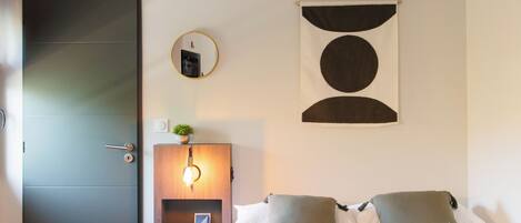 A hotel room with a bed, a bedside table with a lamp, a wall-mounted mirror, and a door.