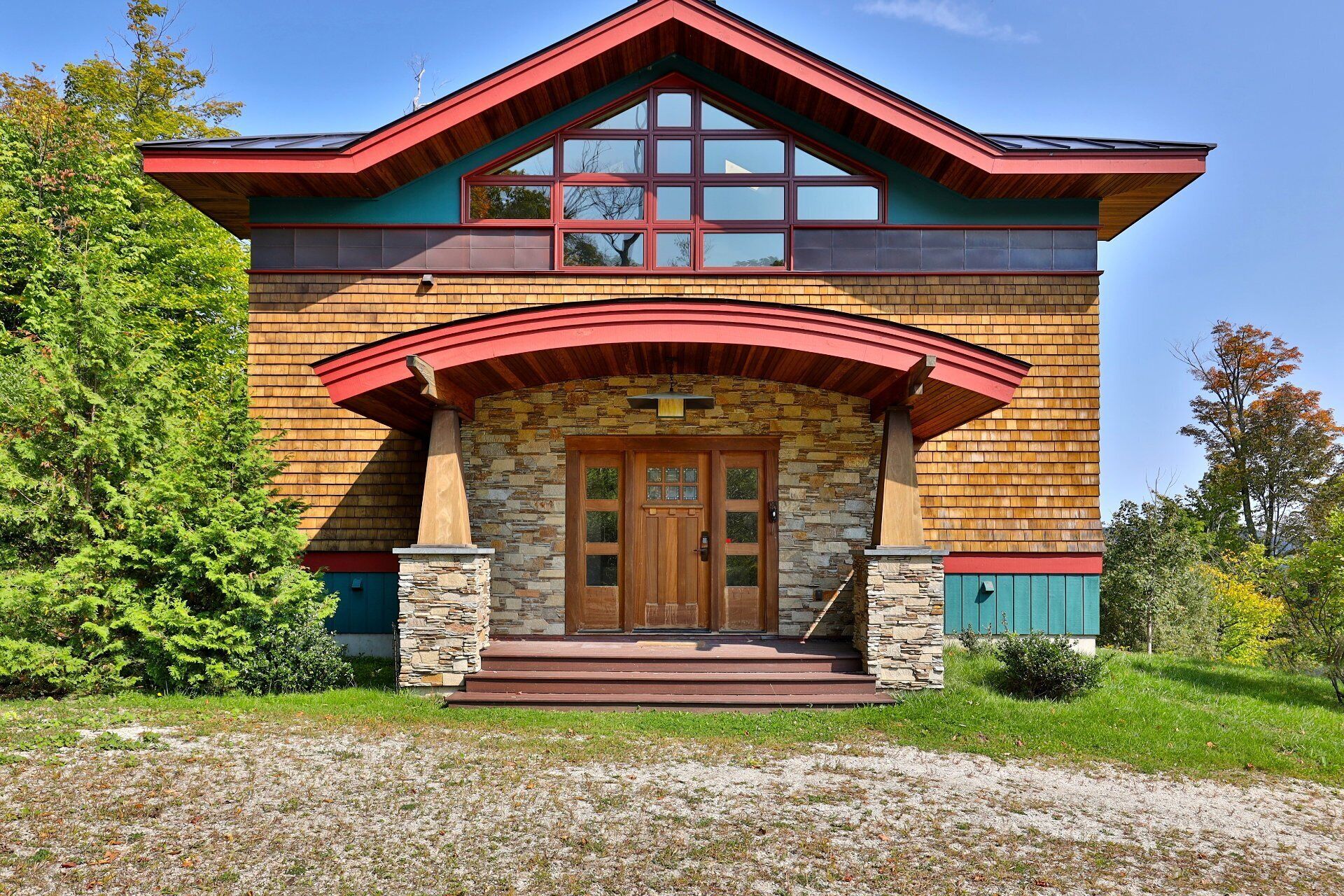 A two-story house with a stone facade, a wooden front porch, and a red roof.