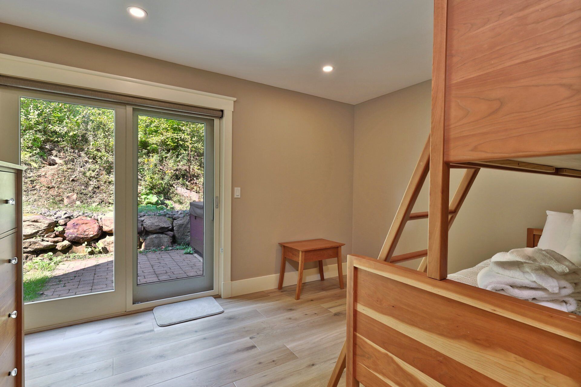 Une pièce avec un lit superposé en bois, une petite table en bois et une porte-fenêtre coulissante donnant sur un jardin agrémenté de rochers et de verdure.