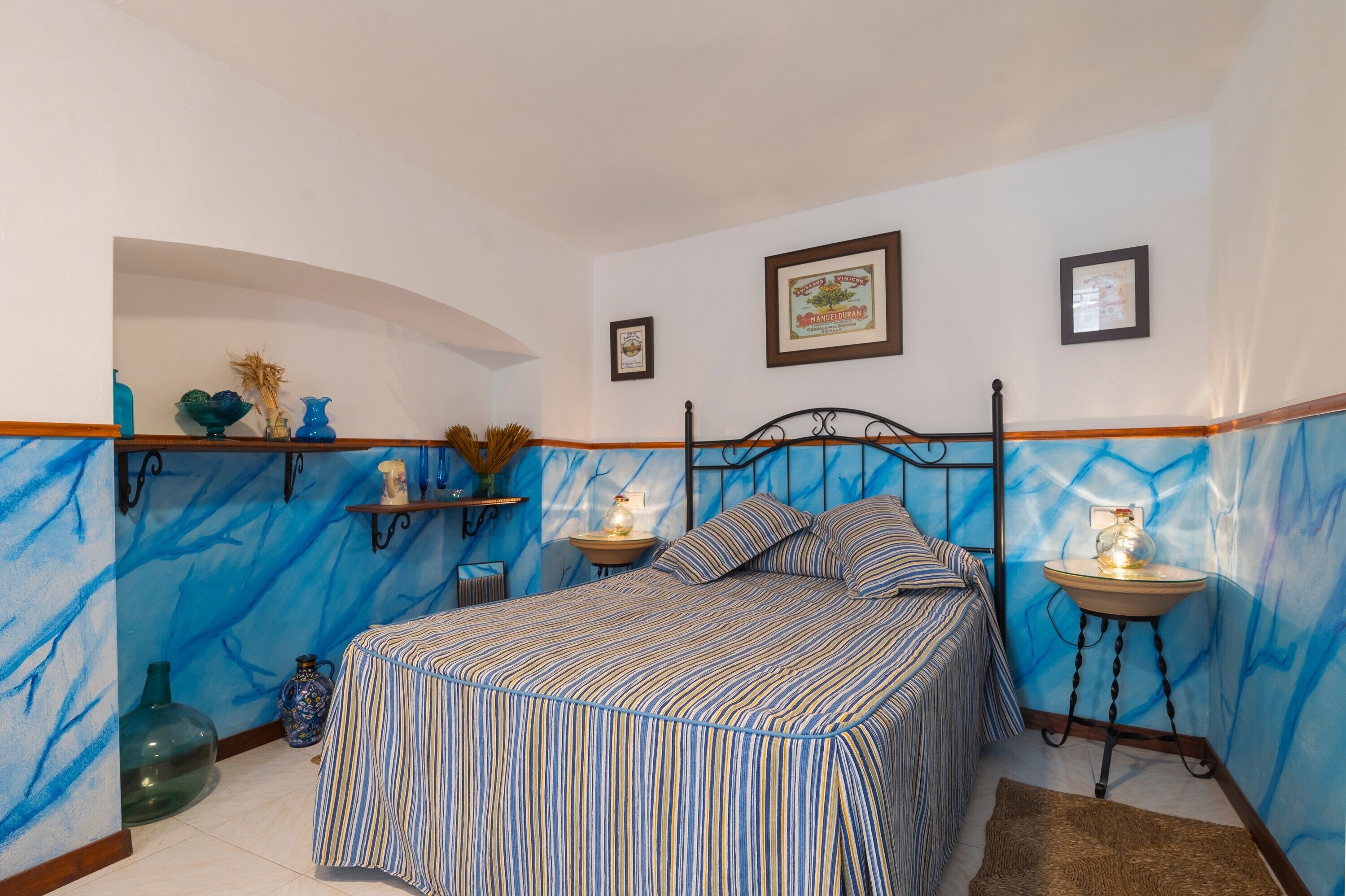 A bedroom with a bed, two bedside tables, a wall-mounted shelf, and a large vase.