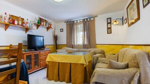 A living room with a television, sofa, dining table, and shelves with bottles. - Country House 'Fuente Nueva' with Balcony (Cazalla de la Sierra)
