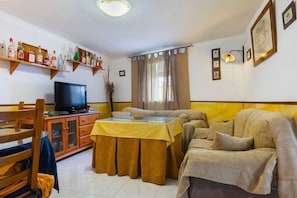 Uma sala de estar com televisão, sofá, mesa de jantar e prateleiras com garrafas.