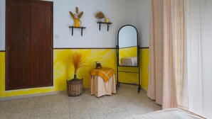 A room with a wooden door, a mirror, a yellow wall, a small table with a yellow cloth, and a striped curtain. - Country House 'Fuente Nueva' with Balcony (Cazalla de la Sierra)