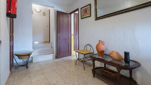 A hallway with a fire extinguisher, a chair, a table with a vase, and a mirror on the wall. - Country House 'Fuente Nueva' with Balcony (Cazalla de la Sierra)