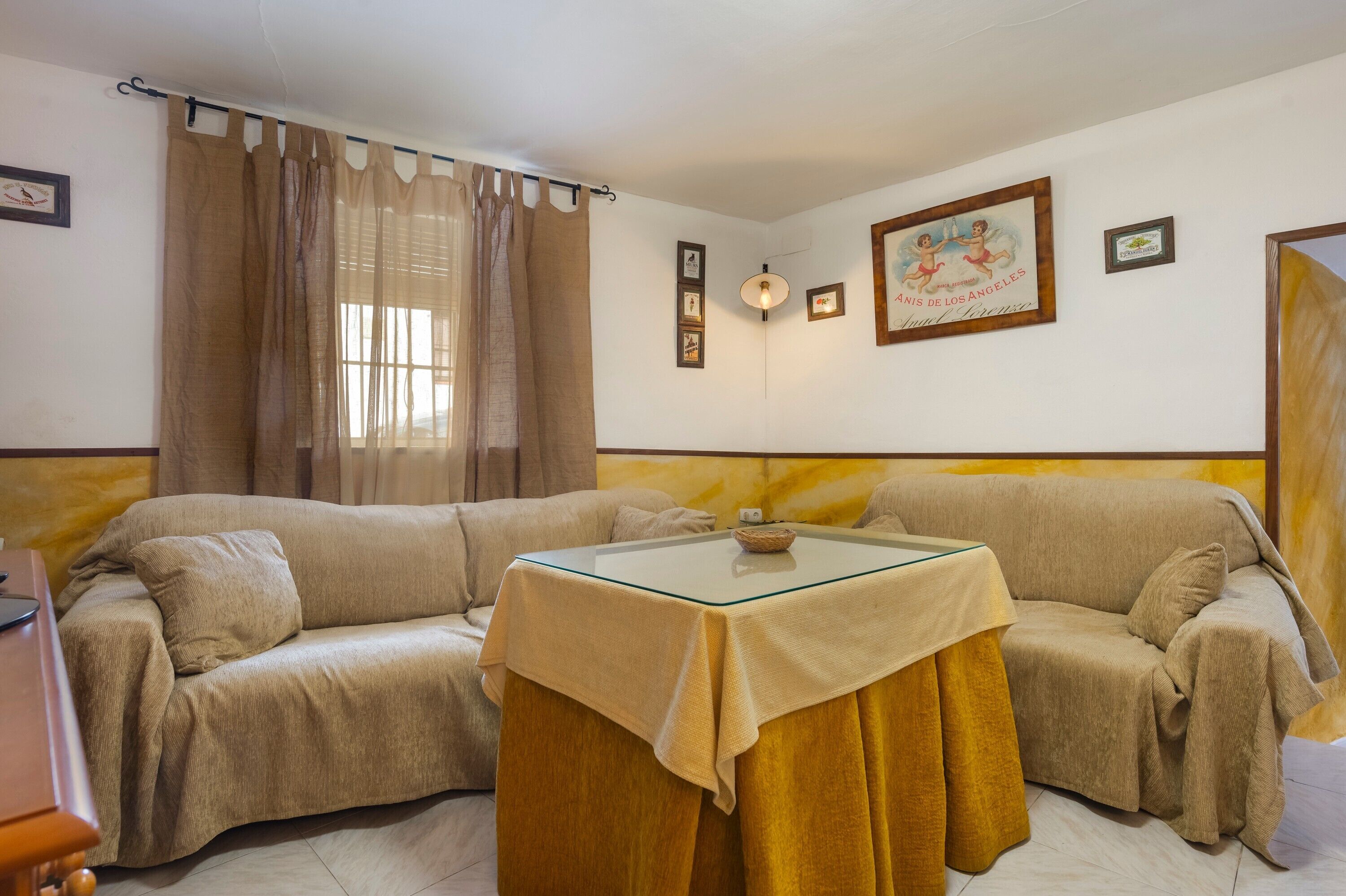 Una habitación con un sofá color crema, una mesa de vidrio y una cortina.