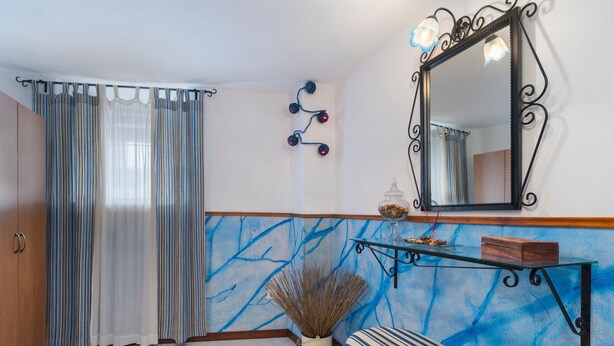 Ein Zimmer mit gestreiftem Vorhang, einem Spiegel mit dekorativem Rahmen, einem kleinen Tisch mit einer Vase und einer Bank.