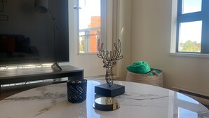 Una sala moderna con un televisor de pantalla plana, una escultura de metal decorativa, una taza estampada y una cesta tejida con un cojín verde.