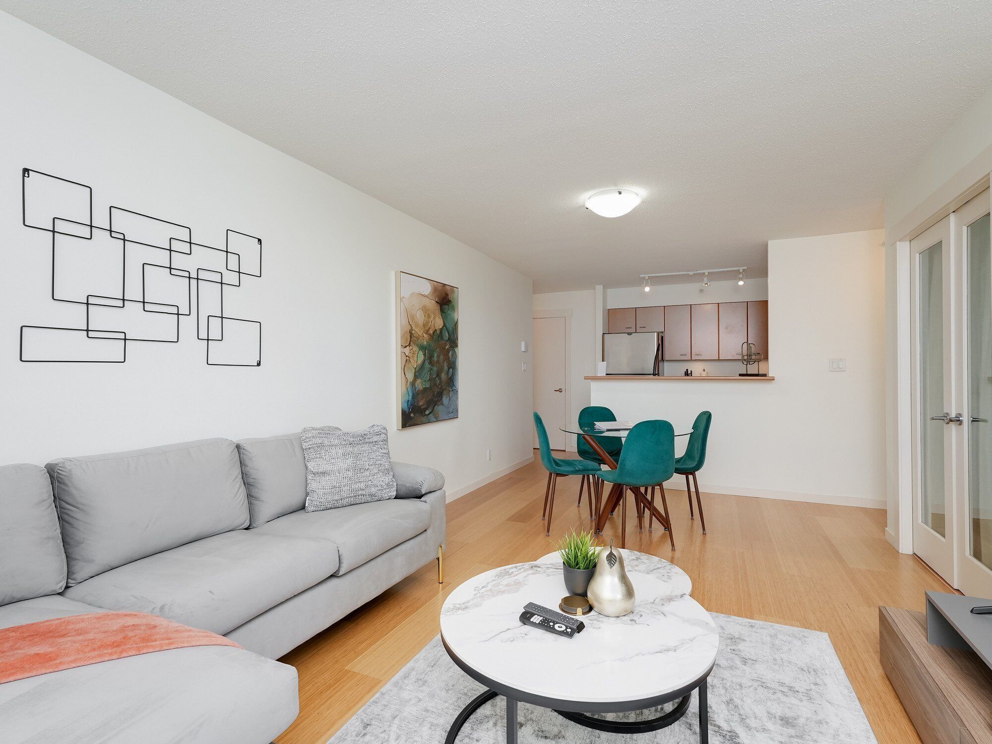 A modern living room with a grey sofa, a round coffee table, and teal chairs.