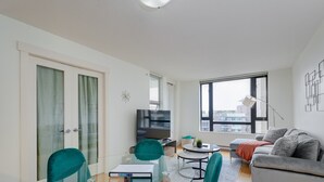 Una sala de estar moderna con puerta de cristal, televisor de pantalla plana, sillas color turquesa, sofá gris y un ventanal grande.