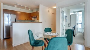 Una cocina moderna con armarios de madera, un refrigerador de acero inoxidable y una mesa de comedor de vidrio con sillas color turquesa.