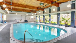 A large indoor swimming pool with a wooden ceiling, clear glass windows, and potted plants around the pool area.