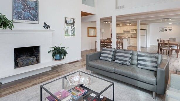 A spacious living room with a fireplace, a grey sofa, and a coffee table with books.