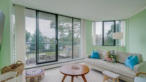 A living room with a sofa, a round wooden table, a small stool, and a wicker basket.
