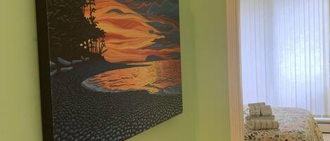 A room with a bed, a painting on the wall, and a window with blinds.