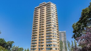 A high-rise residential building with multiple balconies, a car exit, and a parking area.