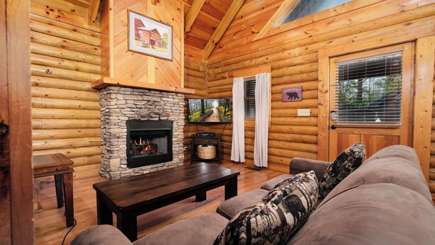 A log cabin interior with a stone fireplace, wooden walls, a sofa, and a television.