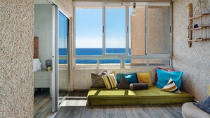Una habitación con un ventanal grande, un sofá verde y una estantería de madera con objetos decorativos.