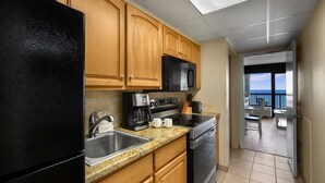 A kitchen with wooden cabinets, a black refrigerator, a microwave, a coffee maker, and a stove. There is a view of a balcony with a table and chairs. - Beach Bum Paradise 14th Flr Oceanfront King Suite (Myrtle Beach)
