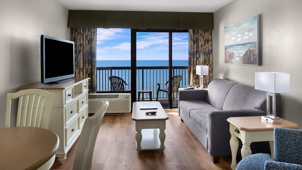 A hotel room with a balcony, a television, a sofa, a dining table, and a chair. - Beach Bum Paradise 14th Flr Oceanfront King Suite (Myrtle Beach)
