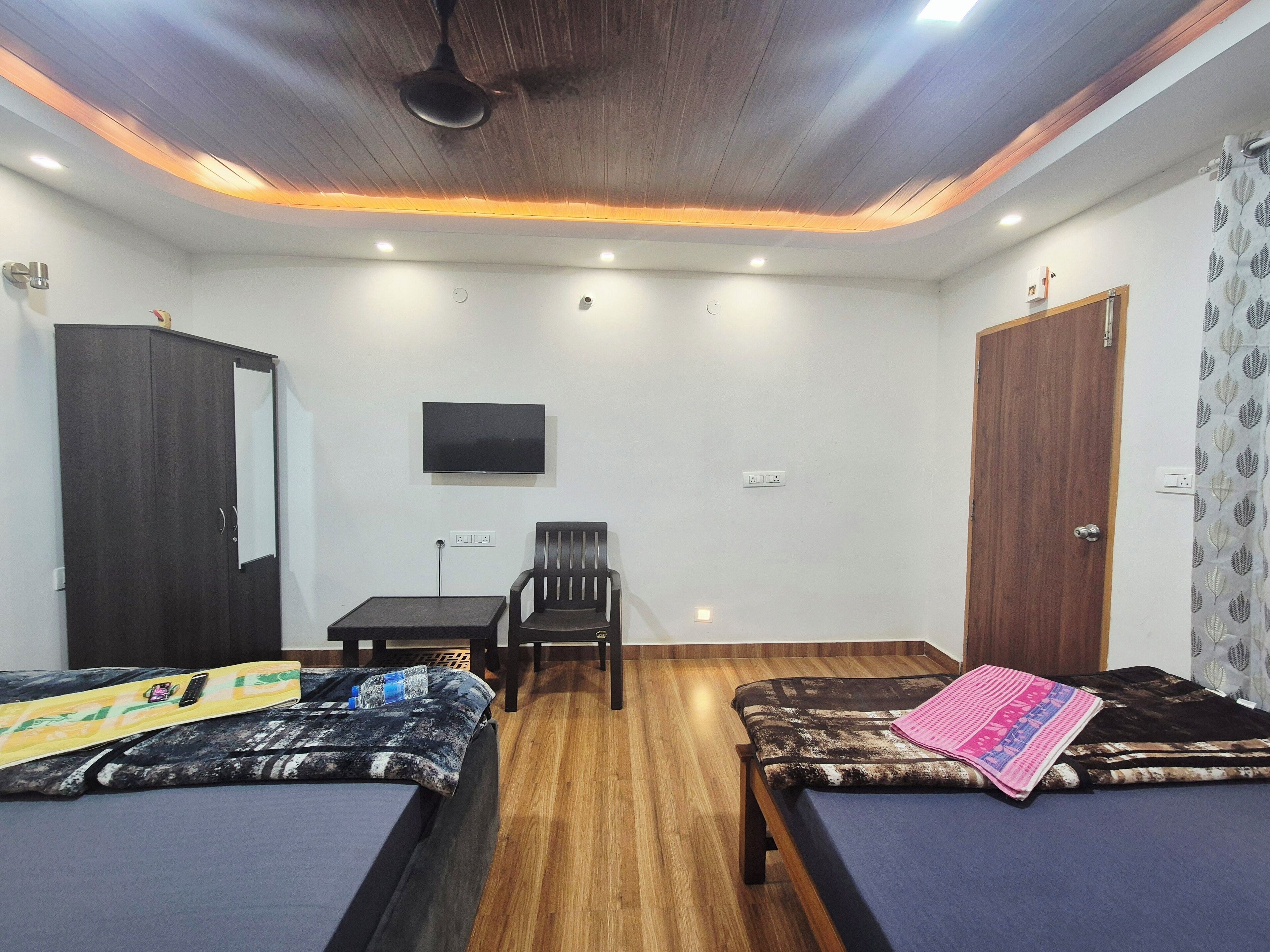 A room with two beds, a desk, a chair, a TV, and a wardrobe.