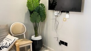 Ein modernes Zimmer mit einem wandmontierten Flachbildfernseher, einer Topfpflanze, einem Sessel und einem Nachttisch mit einem Kopfkissen.