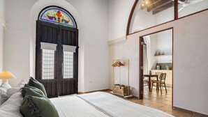 Un dormitorio con una cama grande, una puerta de madera con un vitral y vistas a un comedor.
