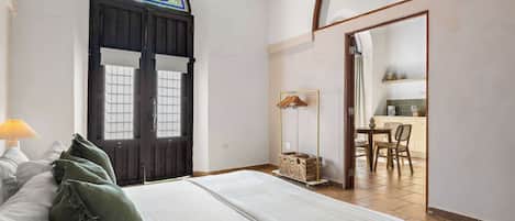 A bedroom with a large bed, a wooden door with a stained glass window, and a view into a dining area.