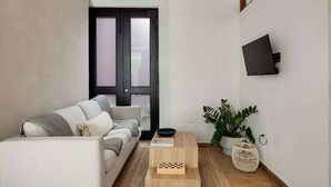 Una sala de estar con un sofá, una mesa de centro, un televisor montado en la pared y una puerta con paneles de vidrio esmerilado.