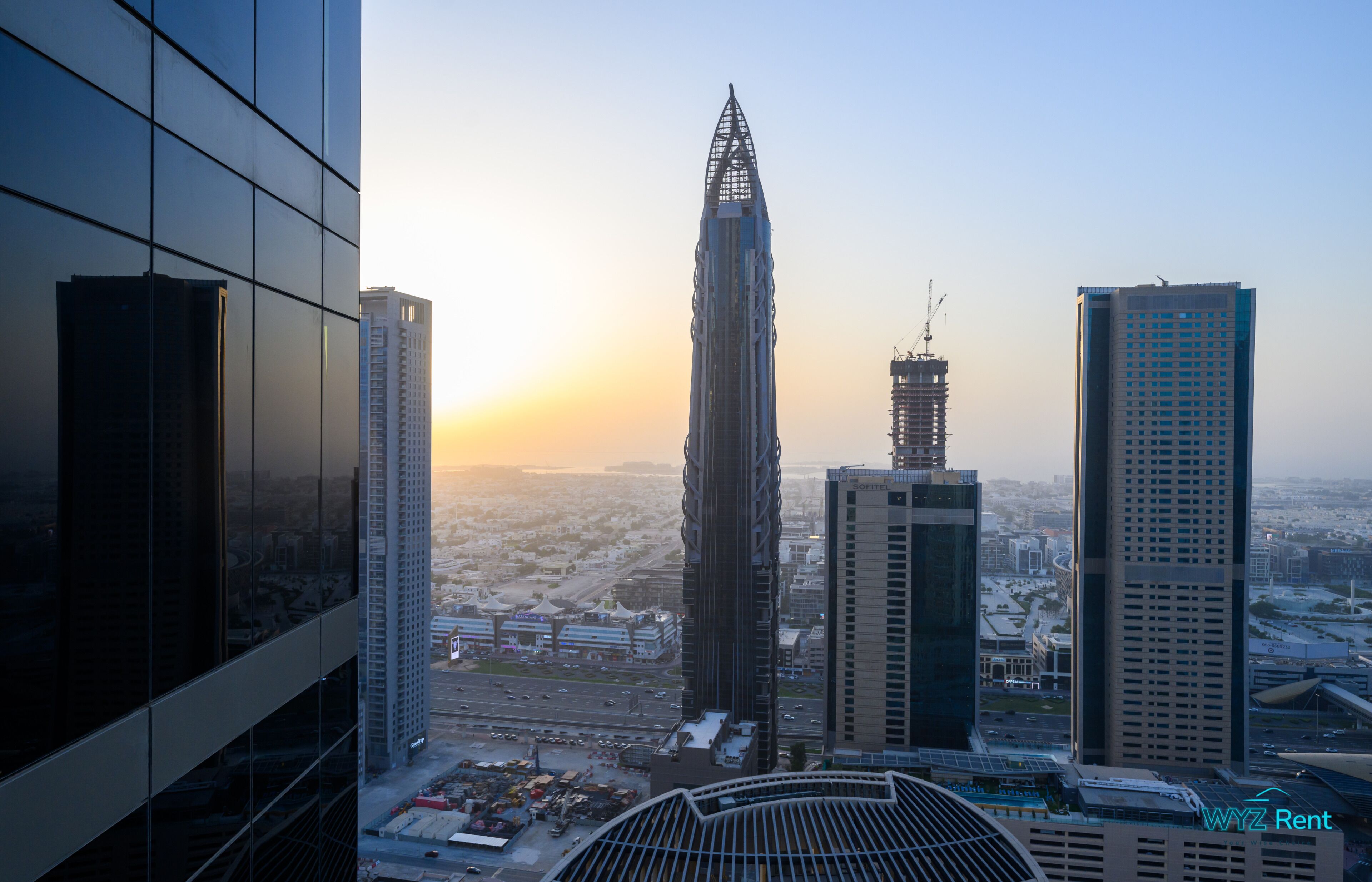 A high-rise building with a unique architectural design, surrounded by other tall buildings and a clear sky.