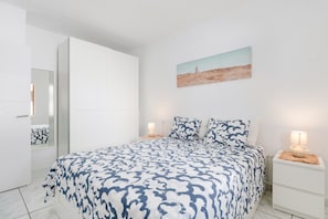 Une chambre à coucher avec un lit, une table de chevet, une lampe, un miroir et un tableau accroché au mur.