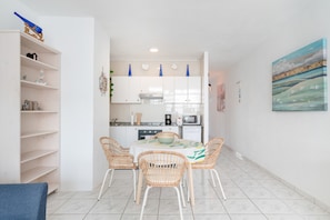 Une cuisine moderne avec des meubles blancs, une table à manger entourée de chaises en osier et un tableau accroché au mur.