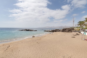 Une plage avec un ciel dégagé, une eau calme et des affleurements rocheux.