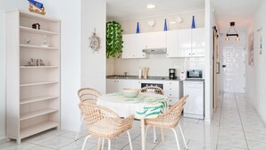 A modern kitchen with white cabinets, a dining table with wicker chairs, and a small island with a microwave.