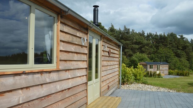 Une cabane en bois avec une porte, une cheminée et un petit porche.