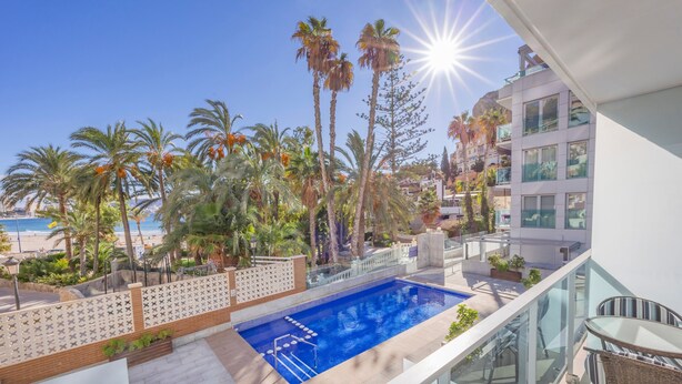 A rooftop pool with a clear view of the beach, surrounded by palm trees and modern buildings.