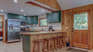 Una cocina moderna con gabinetes de madera, un refrigerador de acero inoxidable, un microondas y una barra con taburetes.