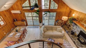 Interior de una cabaña de madera con comedor, sofá, chimenea y ventanas amplias.