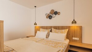 A bedroom with a wooden headboard, a bed with patterned bedding, two pendant lights, and a wall-mounted decorative plate arrangement. - Cozy vacation apartment with unobstructed views of the surrounding mountains (Inzing)