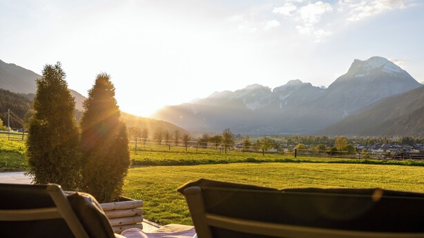A view from a window overlooking a grassy field with mountains in the distance and a chair in the foreground. - Cozy vacation apartment with unobstructed views of the surrounding mountains (Inzing)