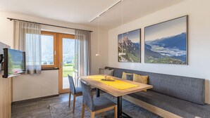 A modern living room with a wooden dining table, grey sofa, and two large landscape paintings. - Cozy vacation apartment with unobstructed views of the surrounding mountains (Inzing)