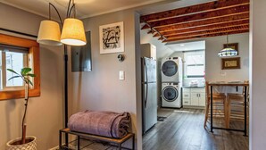 A modern kitchen with a built-in washer and dryer, a wooden dining table, and a bench with a towel. - Private Renovated Apt w/ Washer/Dryer near dwntwn! (Burlington)