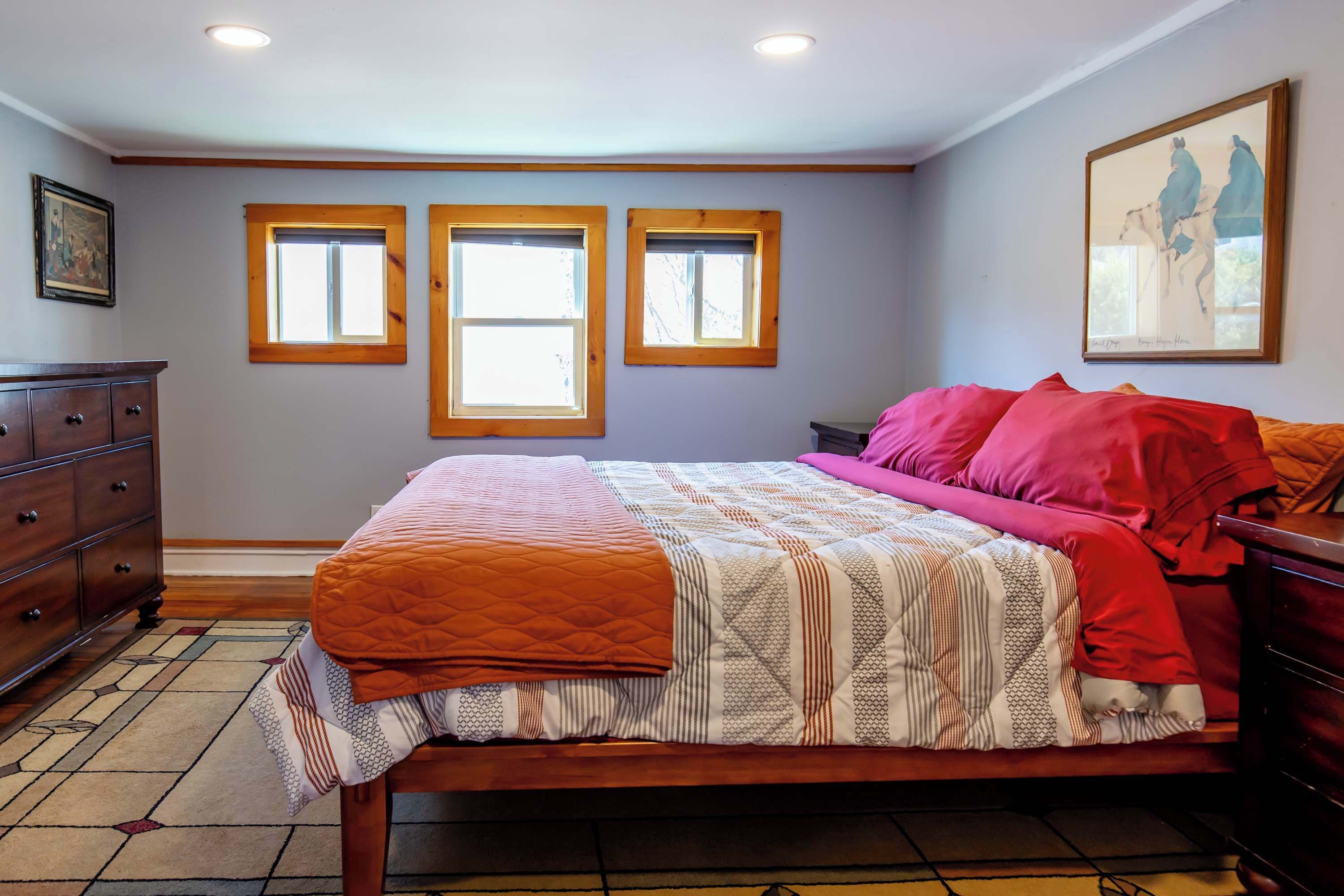 Una camera da letto con un letto, due finestre, una cassettiera e un quadro appeso al muro.