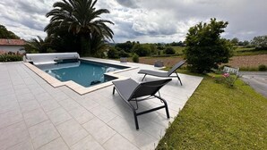 Une piscine dotée de deux chaises longues et d’un banc intégré, entourée d’une pelouse et de palmiers.
