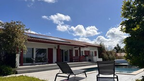 Une maison moderne dotée d’une piscine, de deux chaises longues et d’un espace patio.