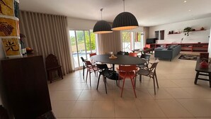 Un salon moderne avec une table à manger ronde, plusieurs chaises et un canapé. Deux suspensions sont fixées au-dessus de la table.