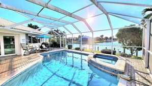 A swimming pool with a glass enclosure, lounge chairs, and a view of a body of water. - Remodeled Waterfront Home w/ Heated Pool  in Punta Gorda (Punta Gorda)