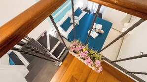 Un escalier avec une rampe en bois, une zone recouverte d’une moquette bleue en contrebas et une composition florale suspendue.
