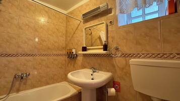 Bany amb banyera, un lavabo i un aparell d'aire acondicionat fixat a la paret.