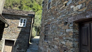 En smal gångstig av sten som löper mellan byggnader med traditionell arkitektur, inklusive en trädörr och ett fönster med fönsterluckor.